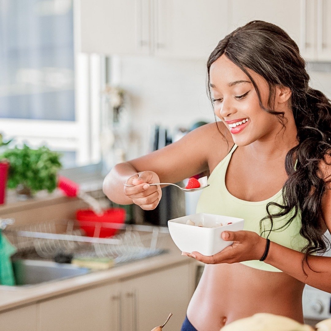 An attractive, smiling, lady eating a from a bowl