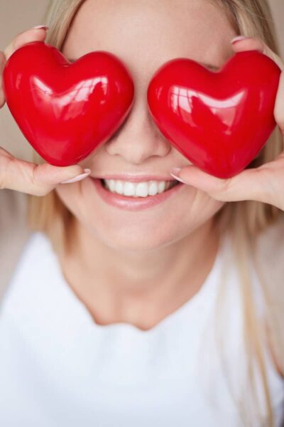 a lady holding red plastic love heart shapes over her eyes feeling in love
